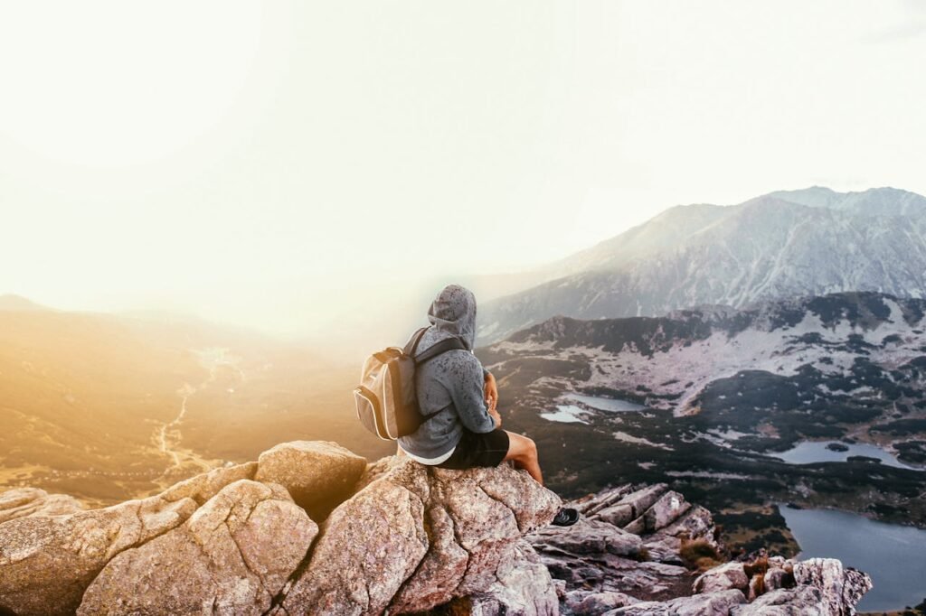 Žmogus su kuprine sėdi ant uolos ir žiūri į kalnų slėnį – fonas blokui „Kaip gauti SEO marketingo paslaugų kainą su pasiūlymu“