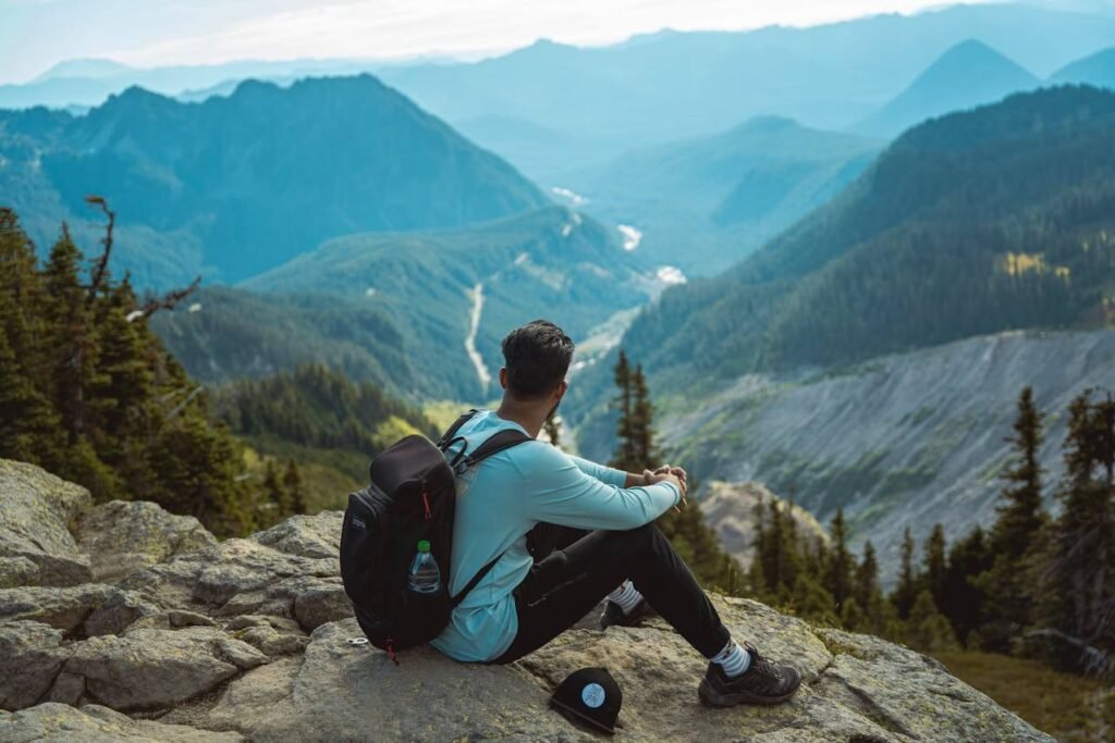 Žmogus su kuprine sėdi ant uolos ir žiūri į kalnų slėnį – metafora profesionalioms SEO specialistų paslaugoms